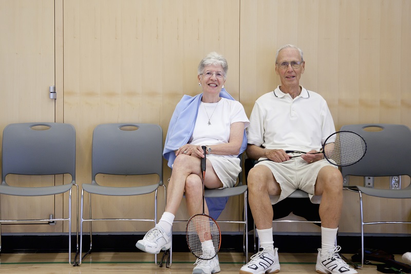 Two older people sitting by a tennis court
