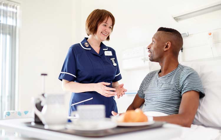 A jovial nurse having conversing with a male patient as they rest in their hospital bed