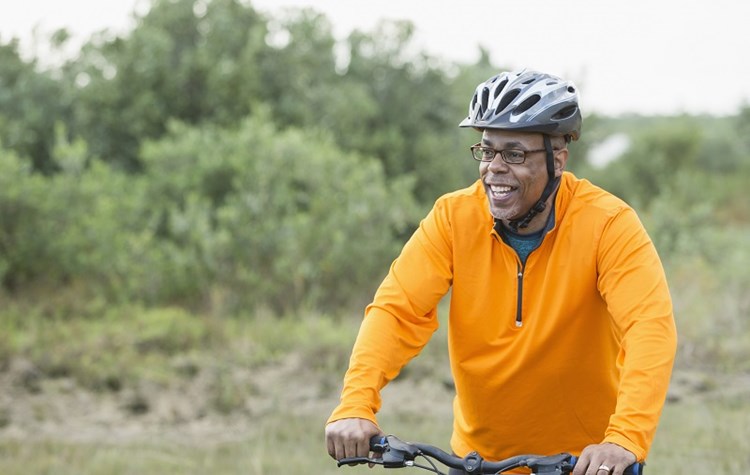 A middle-aged male cyclist wearing a helmet and bright orange shirt, smiling as he rides.
