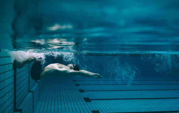 Underwater shot of male swimmer turning over in swimming pool.