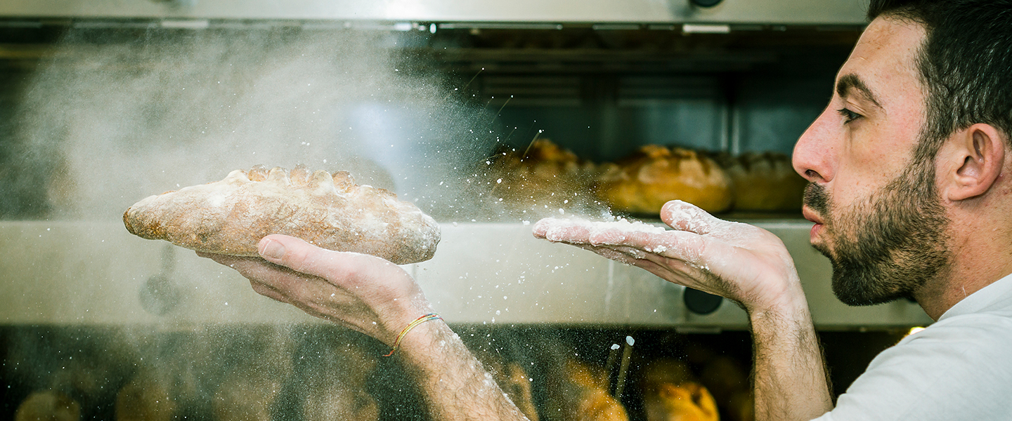 A baker blowing flour on bread