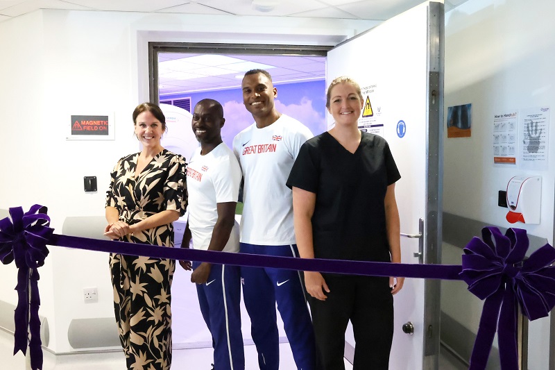 Four people standing behind a ribbon, preparing to cut it