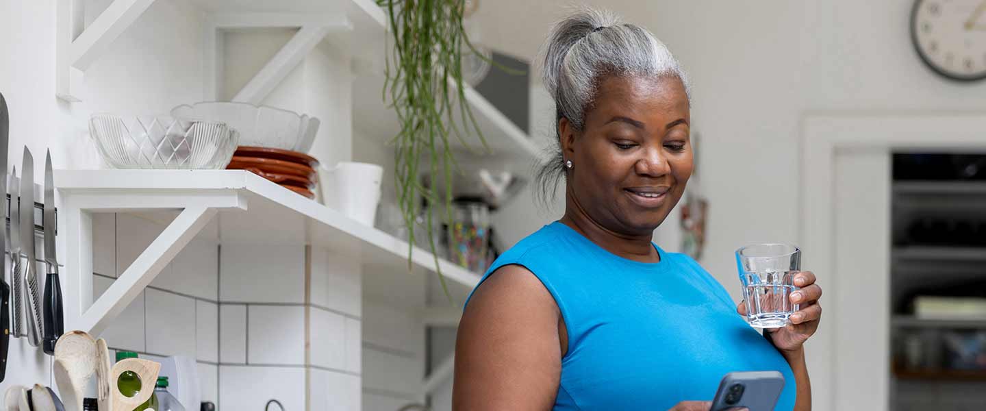 A woman drinking a glass of water and looking at her phone