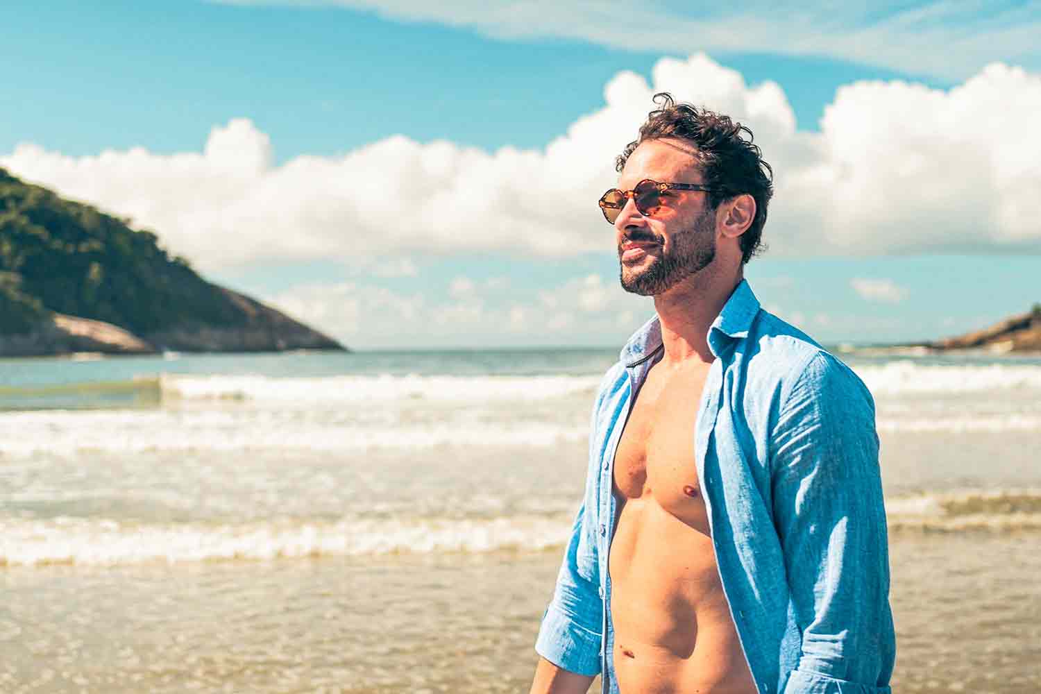 A man on the beach in an open blue shirt