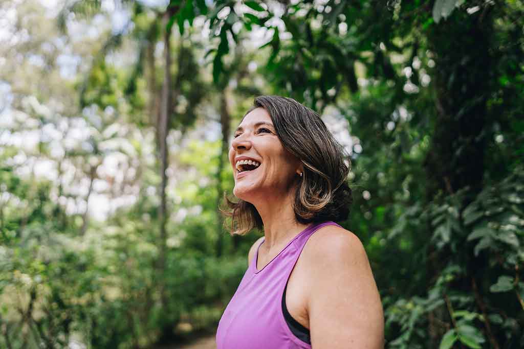 A woman in a pink top smiling in the woods