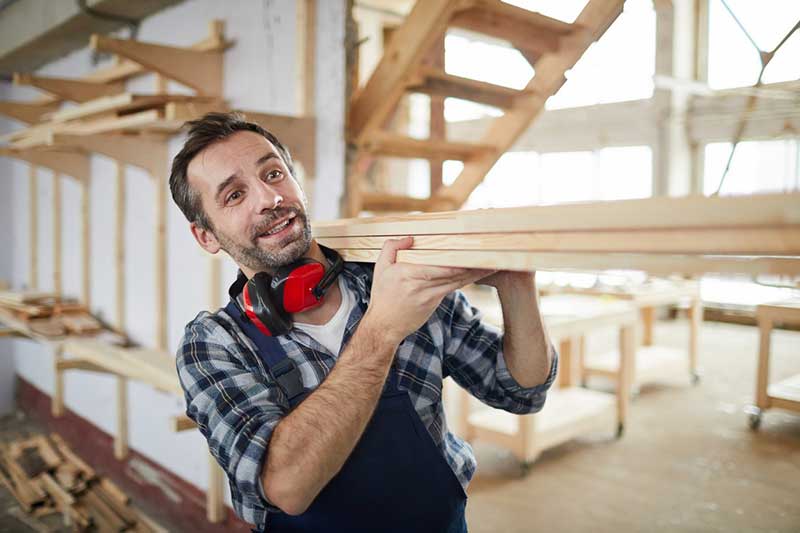 A man carrying a pile of wooden planks on his shoulder