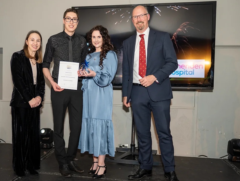 Three people collecting an award from a presenter