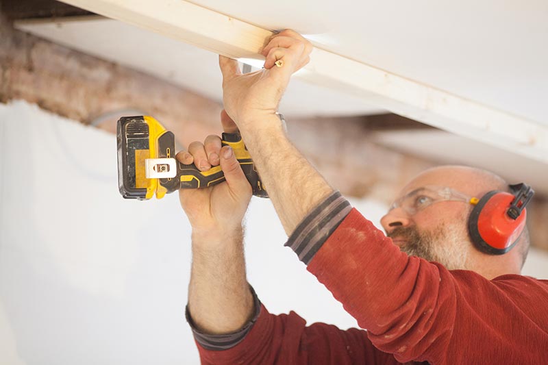 Man attaching wooden beams to a ceiling using a power screwdriver