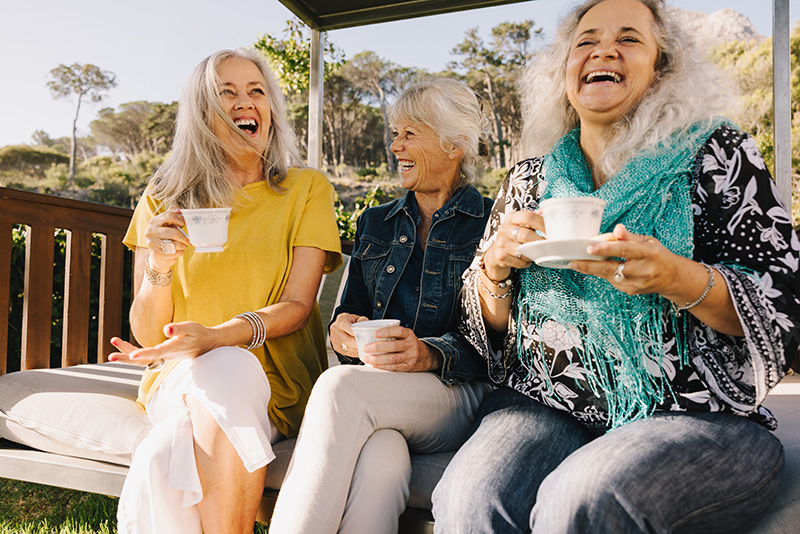 Three senior women laughing while drinking tea