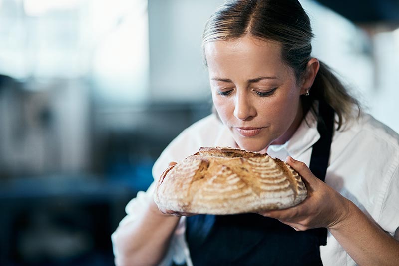 A baker smelling a loaf of freshly cooked bread