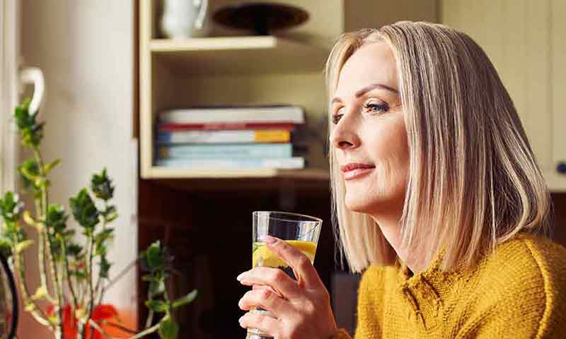 A woman with a glass of water looking out of the window
