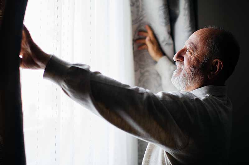 Man opening curtains to let sunlight in